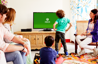 Una familia reunida delante de la tele y la consola Xbox One para jugar.